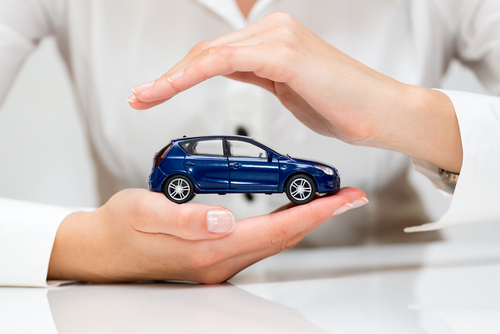 Hands gently cradle a small blue car model, symbolizing care and protection.
