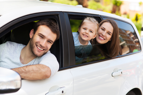 A happy family with a smiling father, mother, and daughter sitting in a car window.
