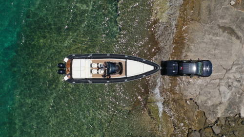 Aerial view of a boat near the shore with a truck parked beside it on rocky terrain.